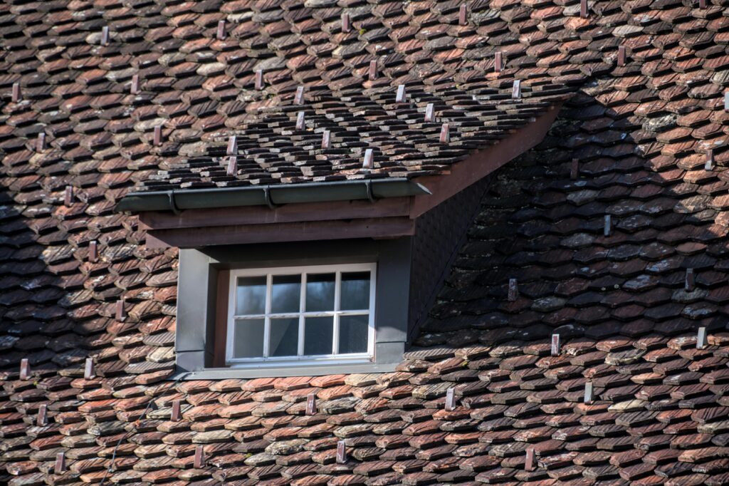 Close-up of a vintage rooftop with a dormer window, showcasing unique tile arrangement and architectural details.