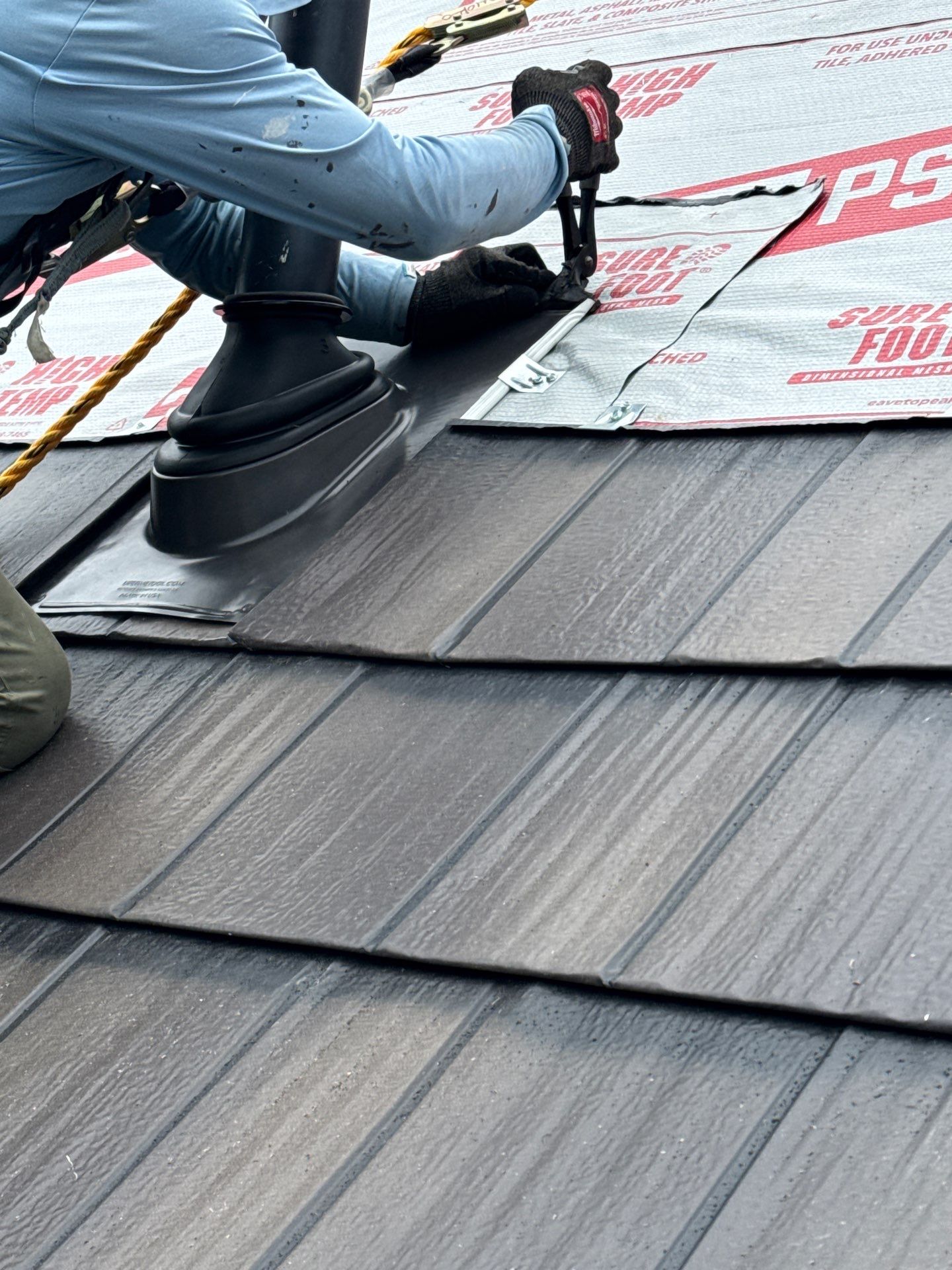 Close-up of a Compass Exteriors installer sealing a black pipe boot on EDCO steel shake shingles, with high-temp underlayment visible behind.